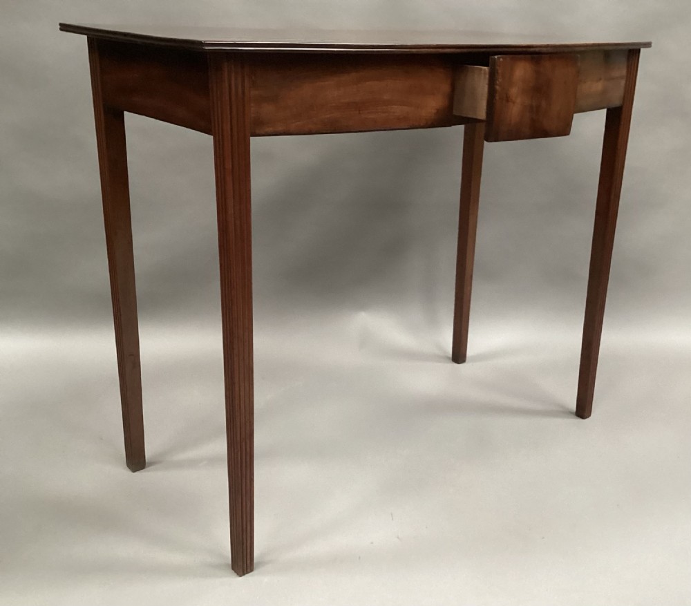 A George III mahogany bow-fronted side table featuring a curved top, frieze panel, and four square tapered legs. View VII