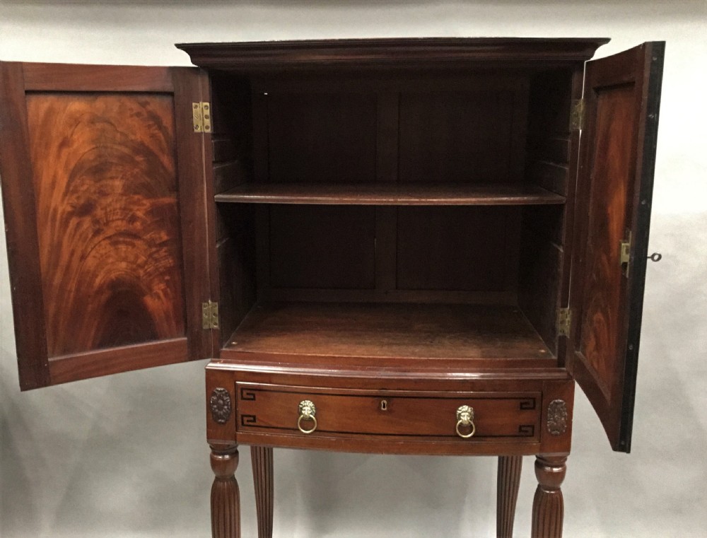 A Regency mahogany cabinet on stand featuring flame mahogany door panels with ebony geometric inlay, a single frieze drawer, reeded legs, and brass paw feet. View III
