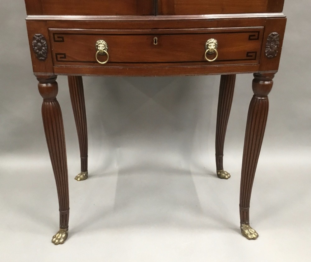 A Regency mahogany cabinet on stand featuring flame mahogany door panels with ebony geometric inlay, a single frieze drawer, reeded legs, and brass paw feet. View XV