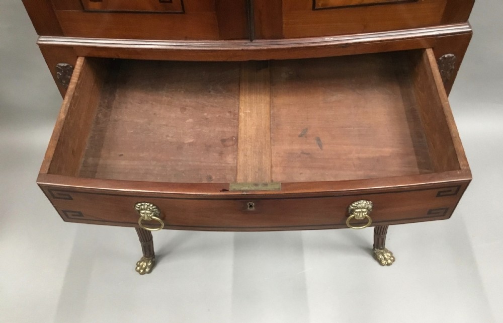A Regency mahogany cabinet on stand featuring flame mahogany door panels with ebony geometric inlay, a single frieze drawer, reeded legs, and brass paw feet. View XVIII