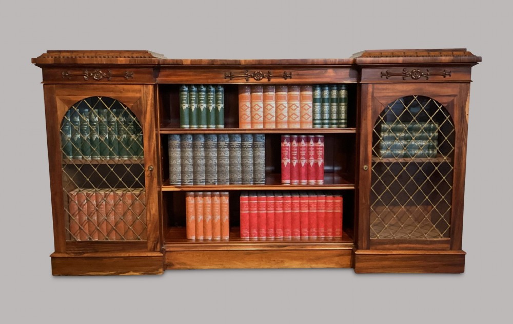 A Regency low inverted breakfront bookcase crafted in Goncalo Alves wood with central open shelving and brass grille side doors. View V