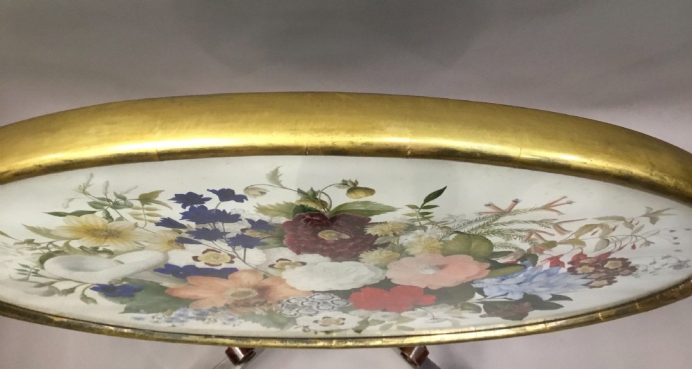 An oval Regency occasional table featuring a hand-painted floral arrangement on the top with a gilt rim, resting on a reeded pedestal stem and carved scroll legs. View XV