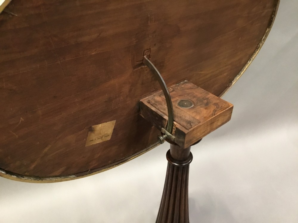An oval Regency occasional table featuring a hand-painted floral arrangement on the top with a gilt rim, resting on a reeded pedestal stem and carved scroll legs. View XVI