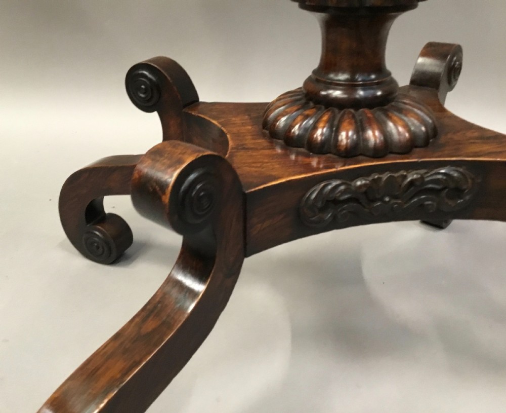 An oval Regency occasional table featuring a hand-painted floral arrangement on the top with a gilt rim, resting on a reeded pedestal stem and carved scroll legs. View XVII