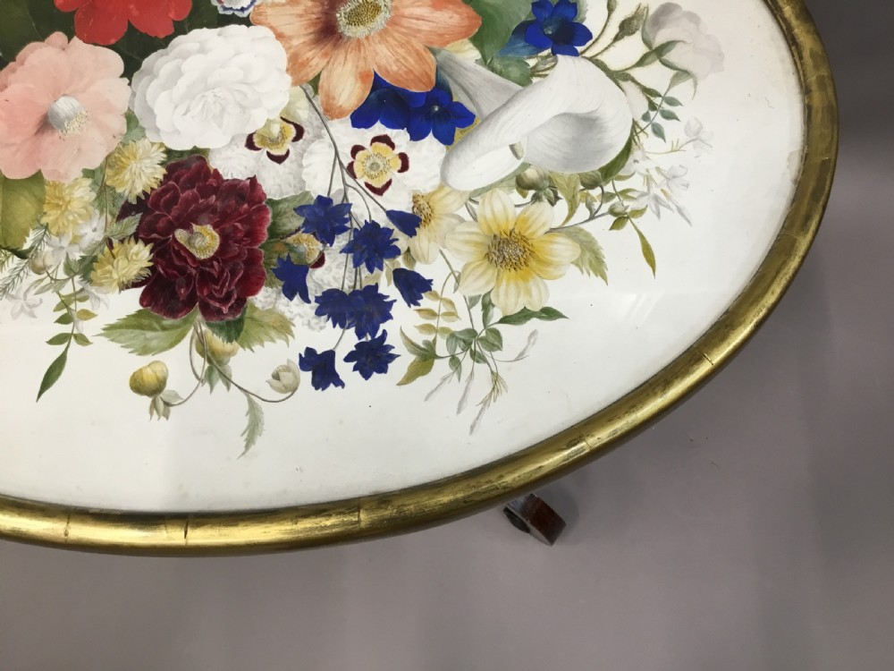 An oval Regency occasional table featuring a hand-painted floral arrangement on the top with a gilt rim, resting on a reeded pedestal stem and carved scroll legs. View XX