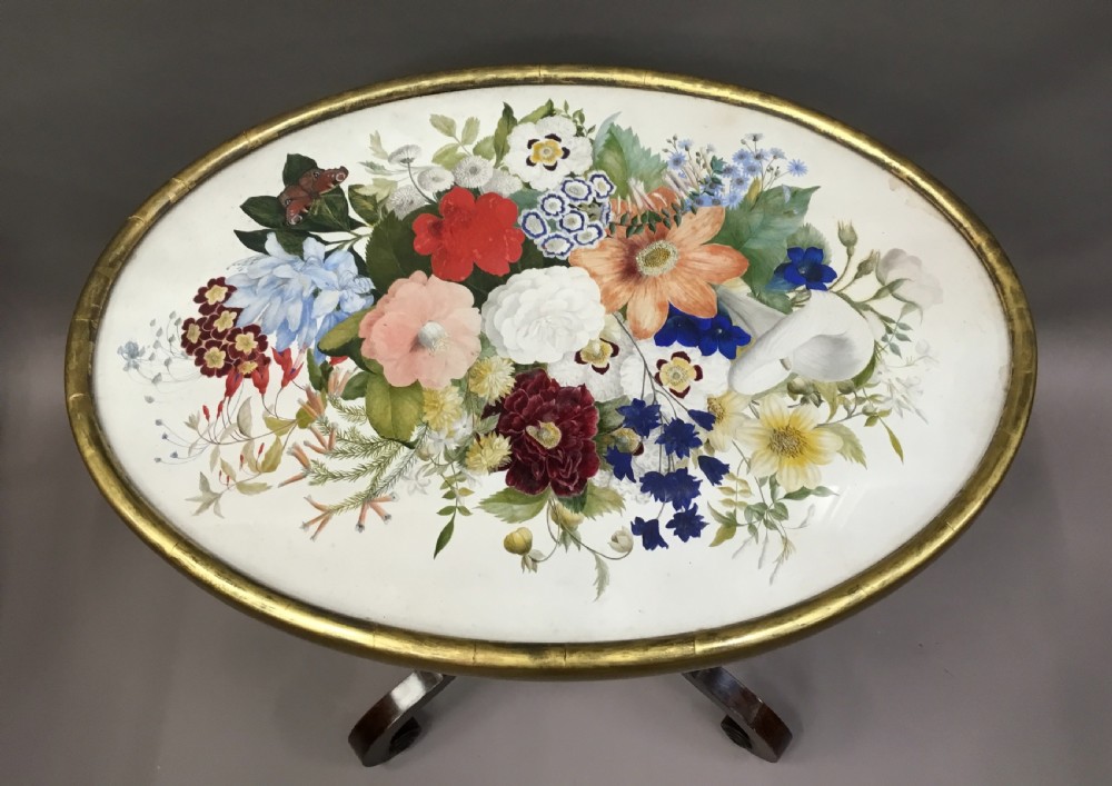 An oval Regency occasional table featuring a hand-painted floral arrangement on the top with a gilt rim, resting on a reeded pedestal stem and carved scroll legs. View XXI