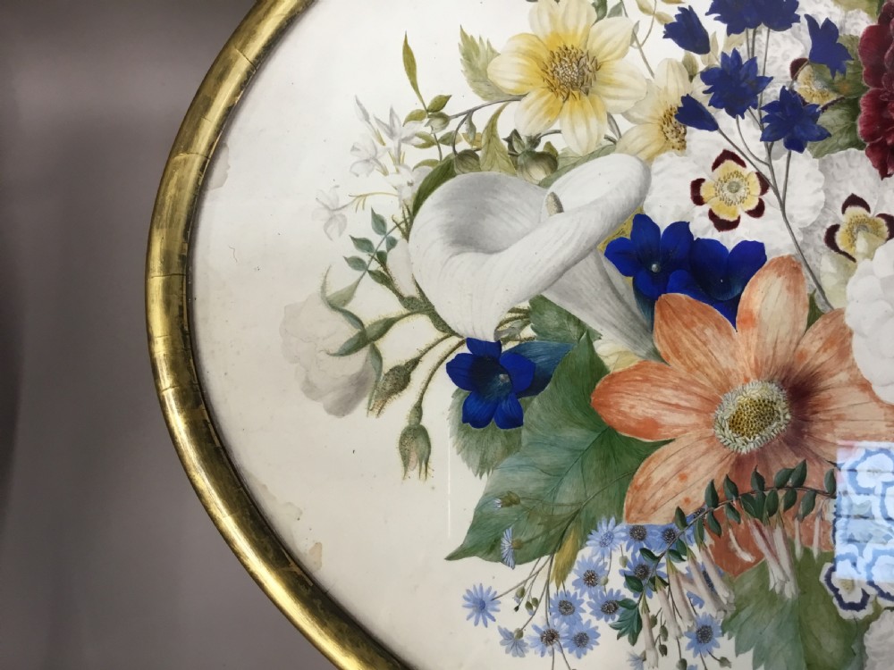 An oval Regency occasional table featuring a hand-painted floral arrangement on the top with a gilt rim, resting on a reeded pedestal stem and carved scroll legs. View XXIV