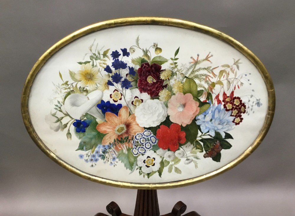 An oval Regency occasional table featuring a hand-painted floral arrangement on the top with a gilt rim, resting on a reeded pedestal stem and carved scroll legs. View XXV
