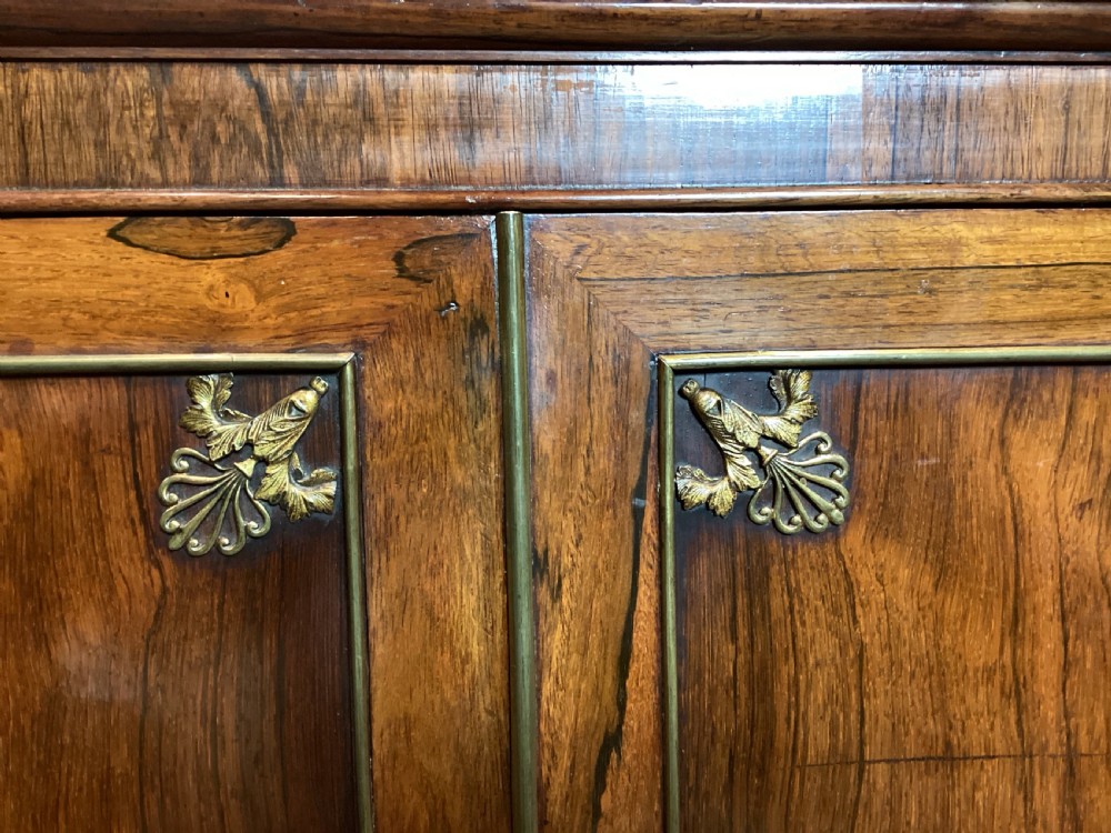 A Regency rosewood side cabinet featuring two panelled doors with brass corner mounts, set beneath a white marble top. View III