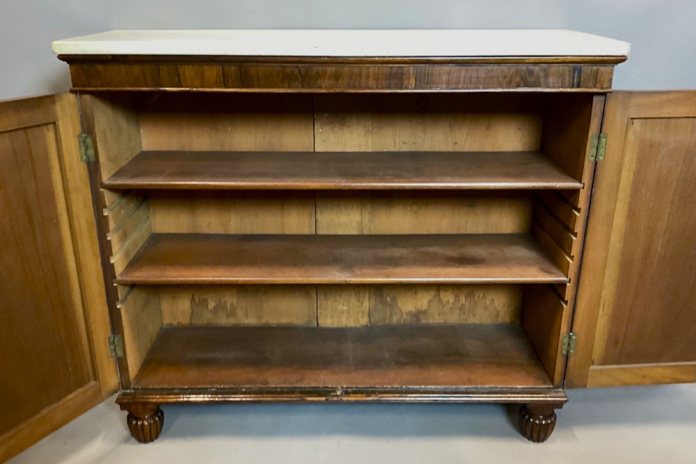 A Regency rosewood side cabinet featuring two panelled doors with brass corner mounts, set beneath a white marble top. View VII