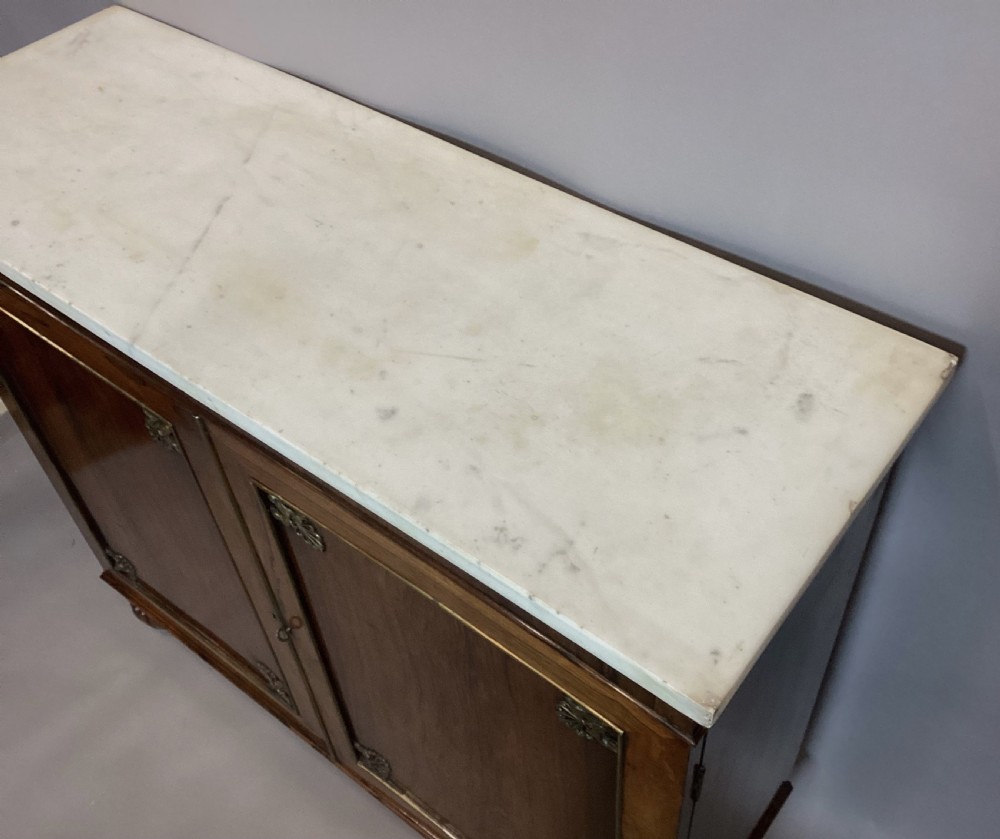 A Regency rosewood side cabinet featuring two panelled doors with brass corner mounts, set beneath a white marble top. View X