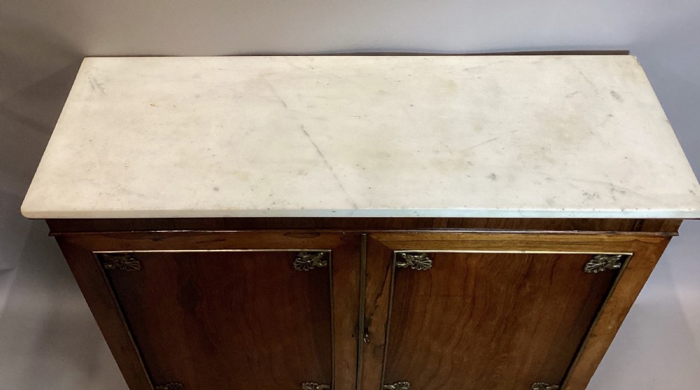 A Regency rosewood side cabinet featuring two panelled doors with brass corner mounts, set beneath a white marble top. View XI