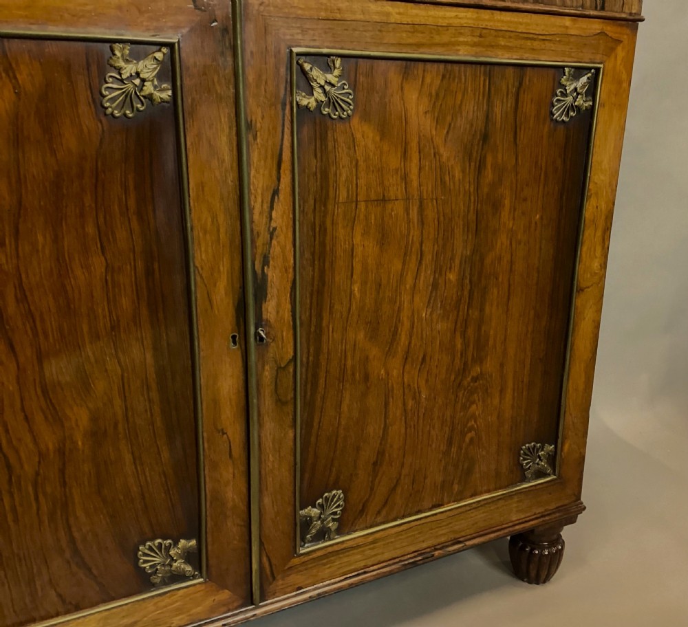 A Regency rosewood side cabinet featuring two panelled doors with brass corner mounts, set beneath a white marble top. View XII