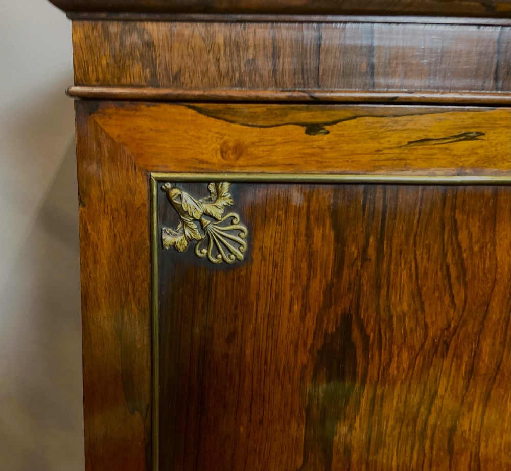 A Regency rosewood side cabinet featuring two panelled doors with brass corner mounts, set beneath a white marble top. View XVI
