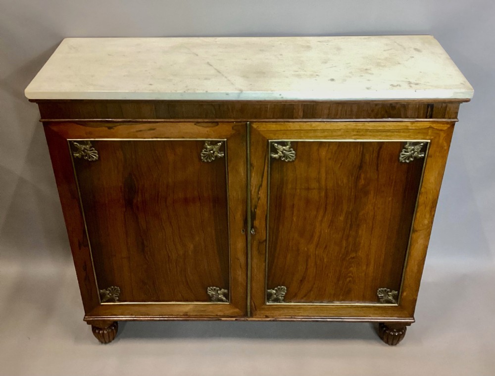 A Regency rosewood side cabinet featuring two panelled doors with brass corner mounts, set beneath a white marble top. View XVIII