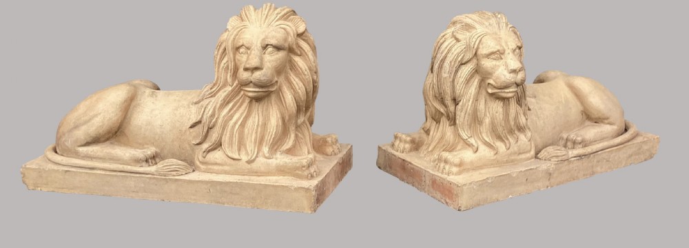 A pair of large nineteenth-century buff terracotta lions depicted in a recumbent position on rectangular bases.