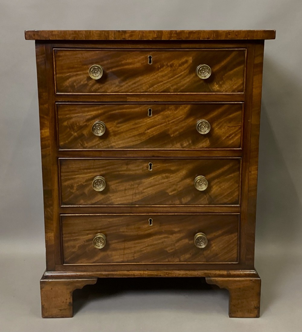 A compact Regency chest of drawers crafted from figured mahogany timber featuring four cockbeaded drawers, brass circular knobs, and traditional bracket feet.