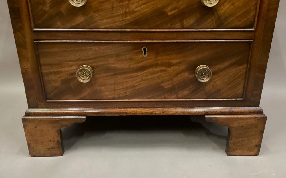 A compact Regency chest of drawers crafted from figured mahogany timber featuring four cockbeaded drawers, brass circular knobs, and traditional bracket feet. View III