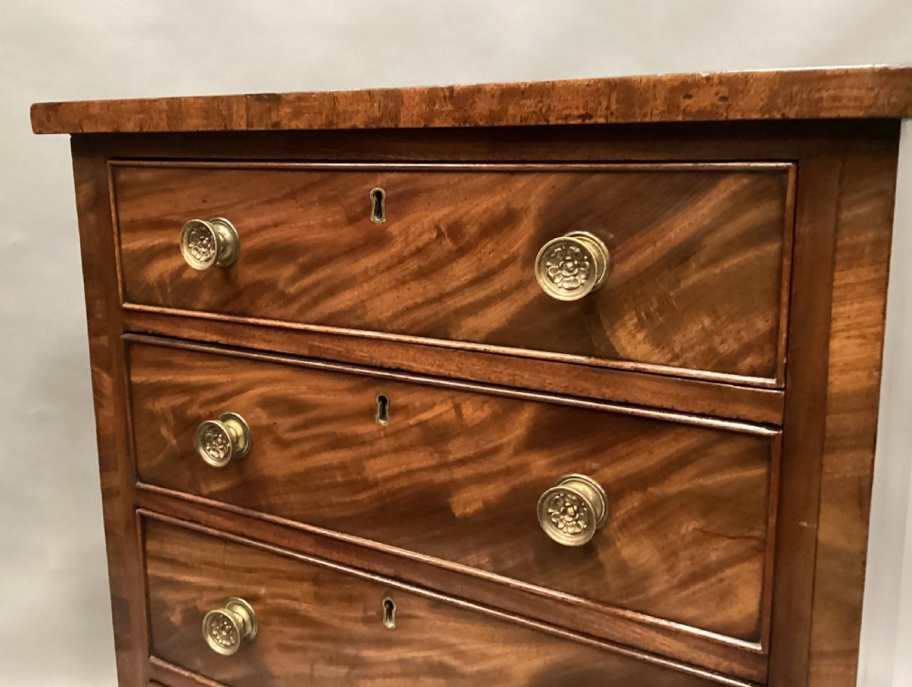 A compact Regency chest of drawers crafted from figured mahogany timber featuring four cockbeaded drawers, brass circular knobs, and traditional bracket feet. View VII