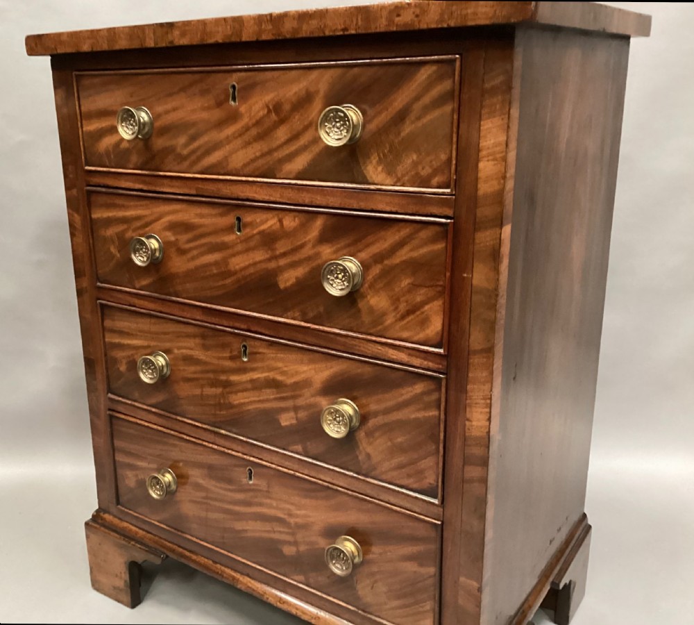 A compact Regency chest of drawers crafted from figured mahogany timber featuring four cockbeaded drawers, brass circular knobs, and traditional bracket feet. View VIII