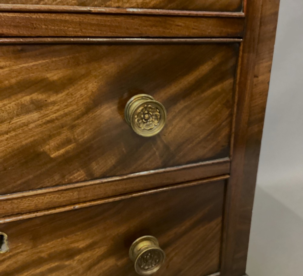 A compact Regency chest of drawers crafted from figured mahogany timber featuring four cockbeaded drawers, brass circular knobs, and traditional bracket feet. View XV