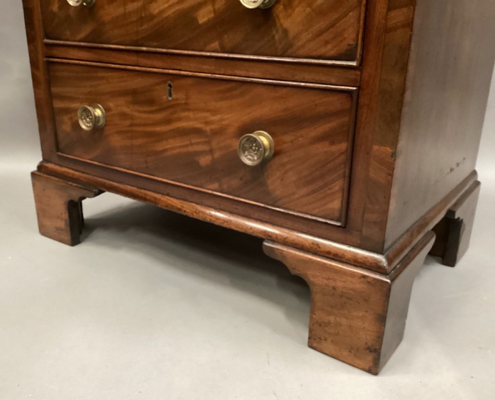 A compact Regency chest of drawers crafted from figured mahogany timber featuring four cockbeaded drawers, brass circular knobs, and traditional bracket feet. View XVI
