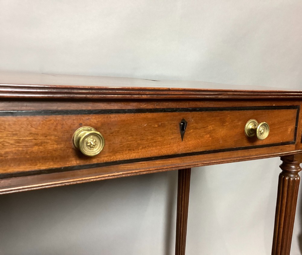 A Regency mahogany chamber writing table featuring an ebony-banded drawer front, reeded turned legs, and brass castors. View VI