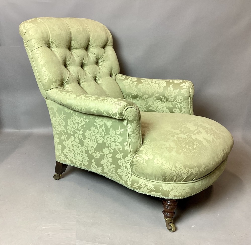 A nineteenth-century Victorian armchair upholstered in sage green floral fabric with a deep button-tufted backrest and turned wooden legs on brass castors.