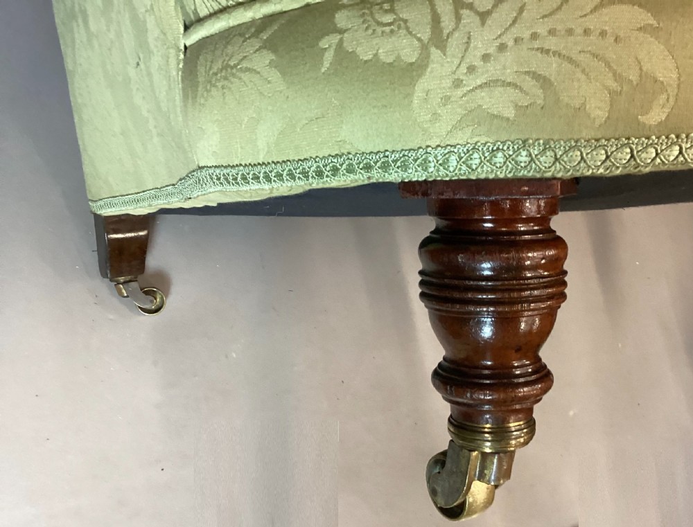 A nineteenth-century Victorian armchair upholstered in sage green floral fabric with a deep button-tufted backrest and turned wooden legs on brass castors. View XI