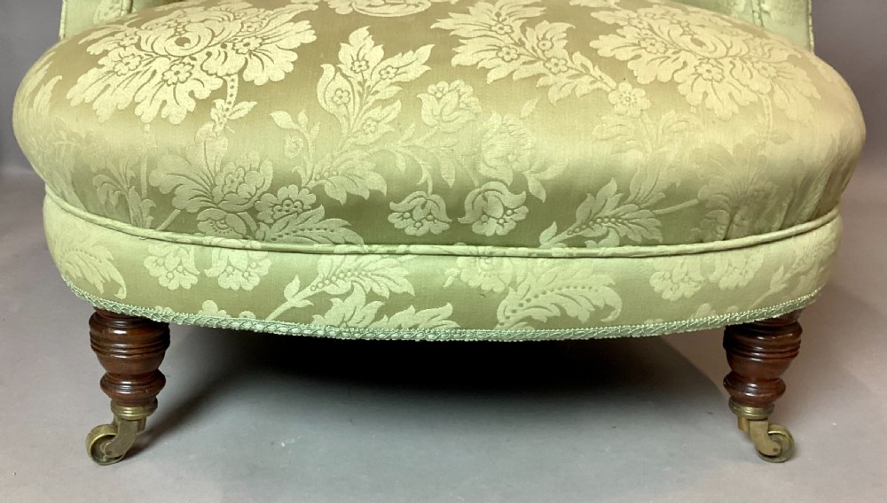 A nineteenth-century Victorian armchair upholstered in sage green floral fabric with a deep button-tufted backrest and turned wooden legs on brass castors. View XV
