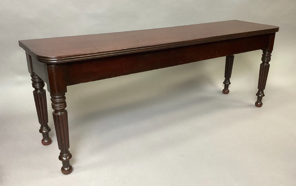 A long Regency mahogany hall bench featuring turned reeded legs, a rectangular solid top with rounded corners, and a polished dark timber finish.