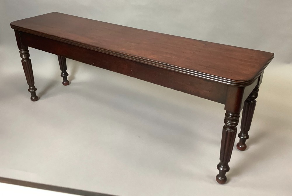 A long Regency mahogany hall bench featuring turned reeded legs, a rectangular solid top with rounded corners, and a polished dark timber finish. View V