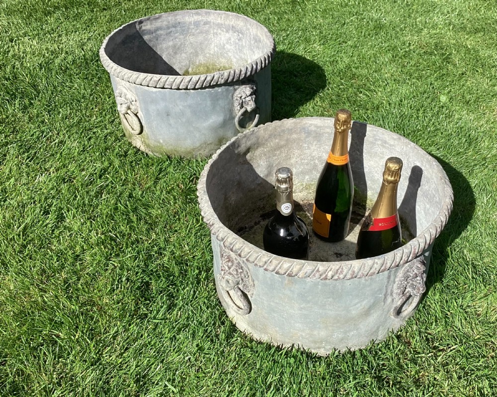 A pair of large cylindrical Regency lead garden planters featuring moulded rope-twist rims and relief lion mask ring handles with a weathered grey patina. View II