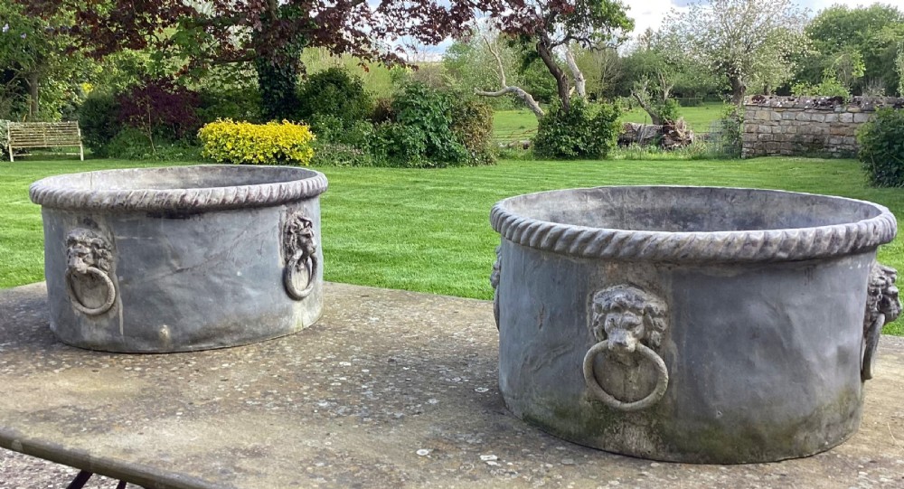 A pair of large cylindrical Regency lead garden planters featuring moulded rope-twist rims and relief lion mask ring handles with a weathered grey patina. View III