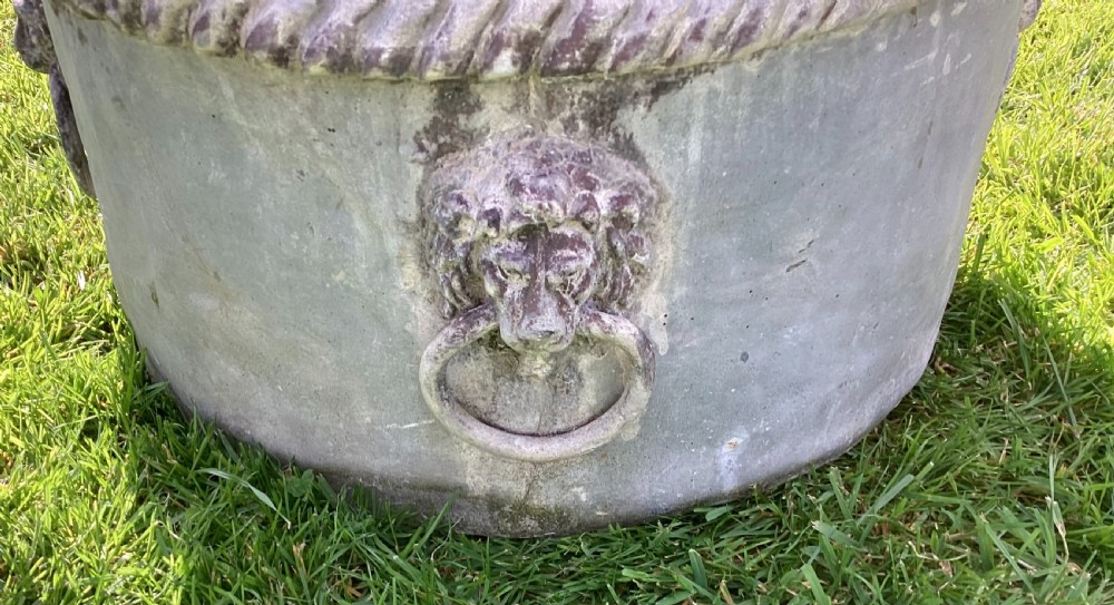 A pair of large cylindrical Regency lead garden planters featuring moulded rope-twist rims and relief lion mask ring handles with a weathered grey patina. View XIV