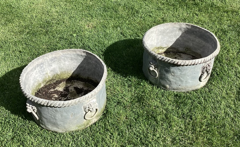 A pair of large cylindrical Regency lead garden planters featuring moulded rope-twist rims and relief lion mask ring handles with a weathered grey patina. View XV