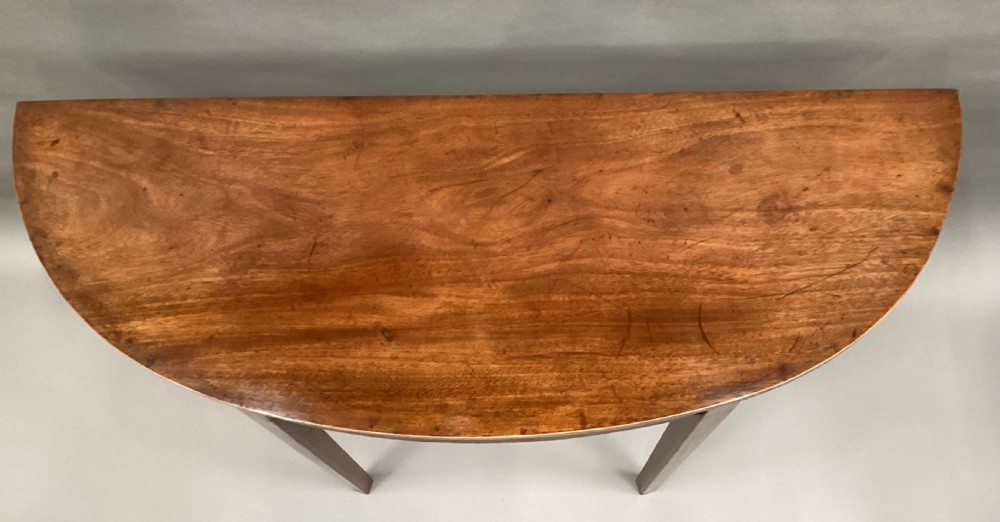 A semi-circular George III style mahogany console table featuring subtle line inlay and four slender square tapered legs. View III