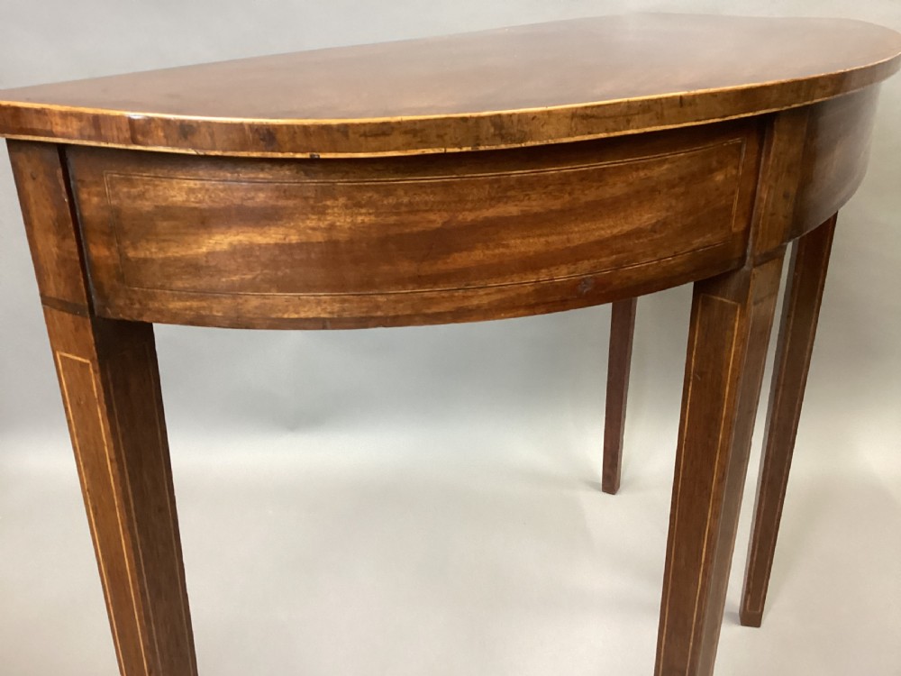 A semi-circular George III style mahogany console table featuring subtle line inlay and four slender square tapered legs. View V