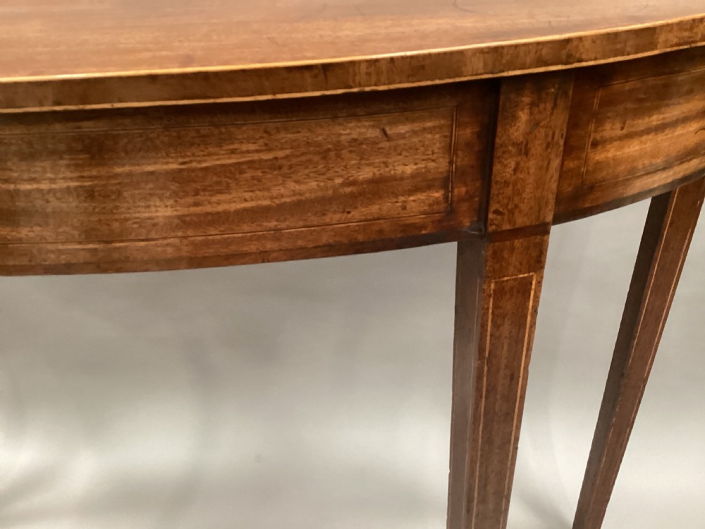A semi-circular George III style mahogany console table featuring subtle line inlay and four slender square tapered legs. View X