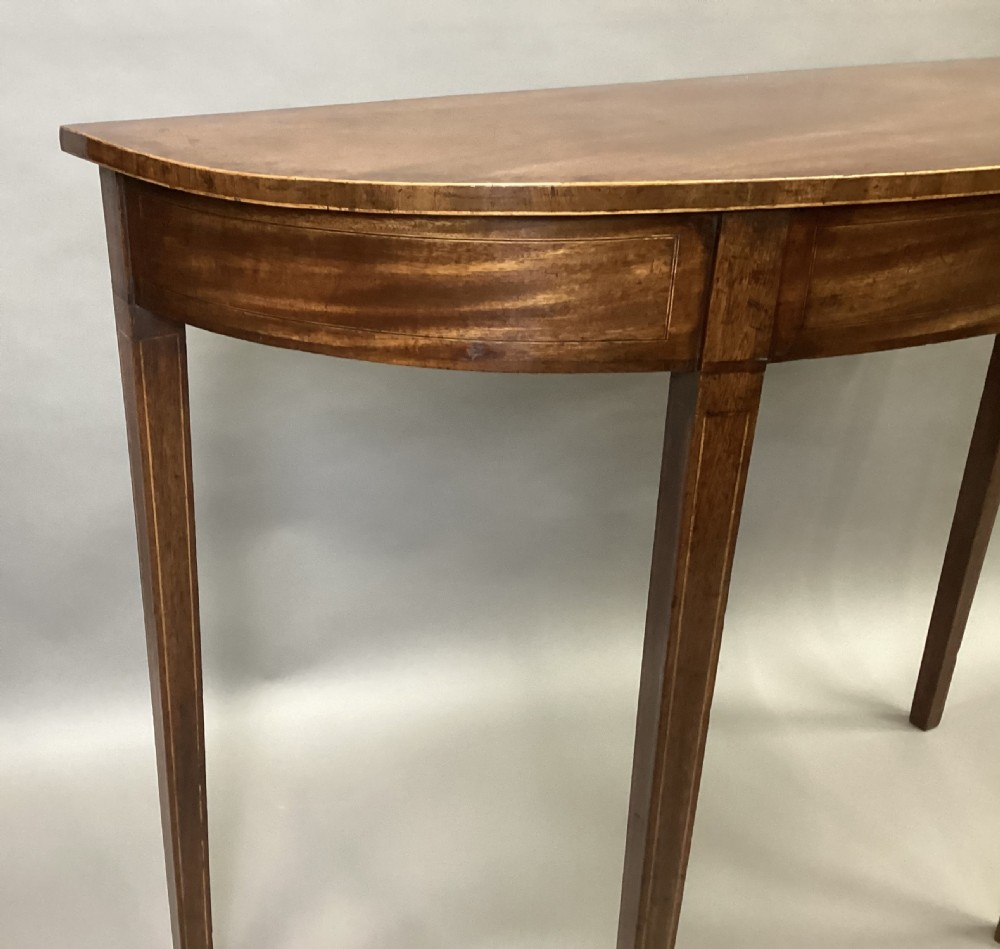 A semi-circular George III style mahogany console table featuring subtle line inlay and four slender square tapered legs. View XI
