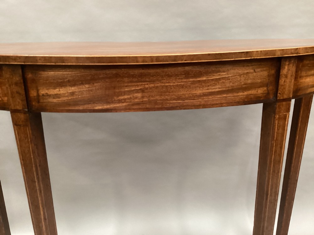 A semi-circular George III style mahogany console table featuring subtle line inlay and four slender square tapered legs. View XII