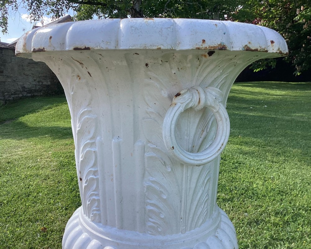 A white painted 19th-century cast iron garden urn with fluted gadrooning, leaf relief carving, side ring handles, and a square pedestal base. View V
