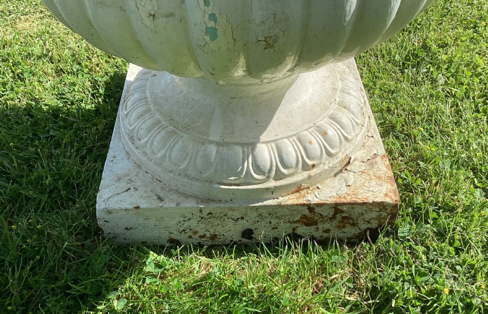 A white painted 19th-century cast iron garden urn with fluted gadrooning, leaf relief carving, side ring handles, and a square pedestal base. View XI