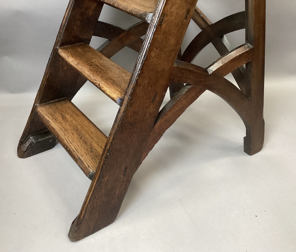 A nineteenth-century dark oak set of Gothic Revival library steps featuring four treads, arched bracing, and a tall vertical handrail. View XIX
