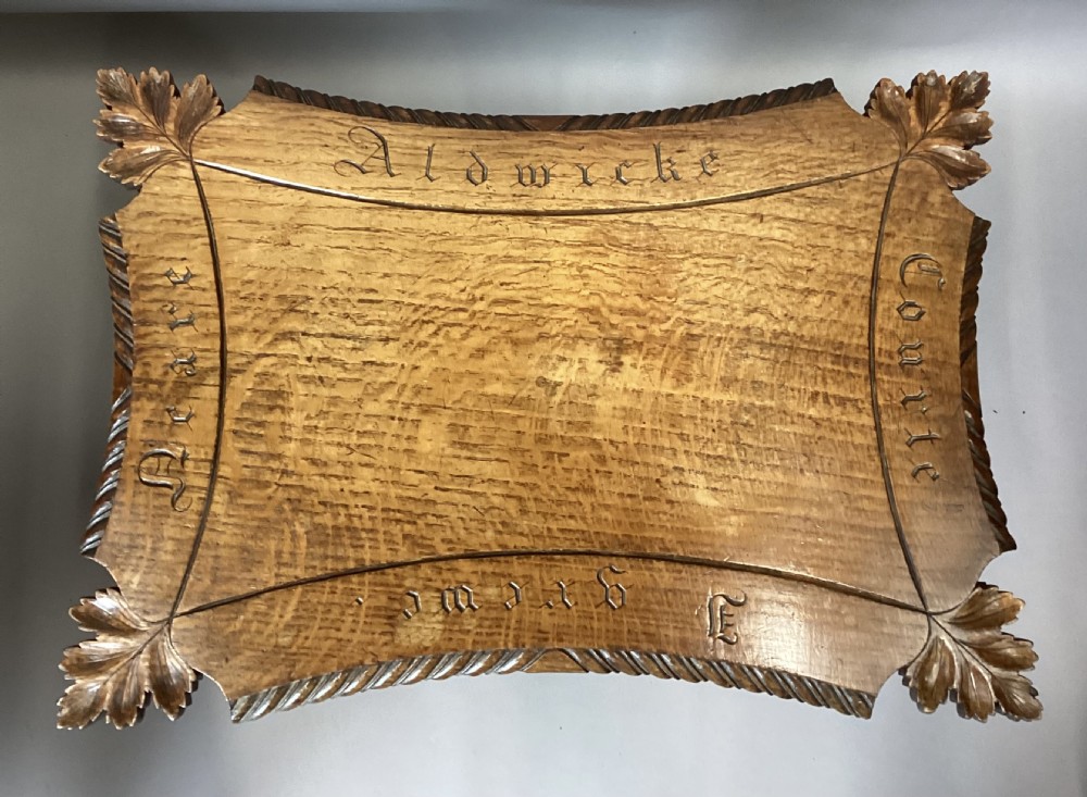 A Regency figured oak occasional table featuring carved acanthus corners, a rope-twist border, incised lettering detail, a turned central stem, and carved legs on castors. View II