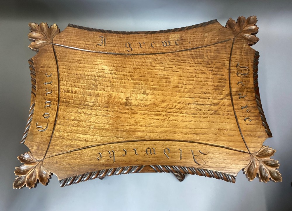 A Regency figured oak occasional table featuring carved acanthus corners, a rope-twist border, incised lettering detail, a turned central stem, and carved legs on castors. View V
