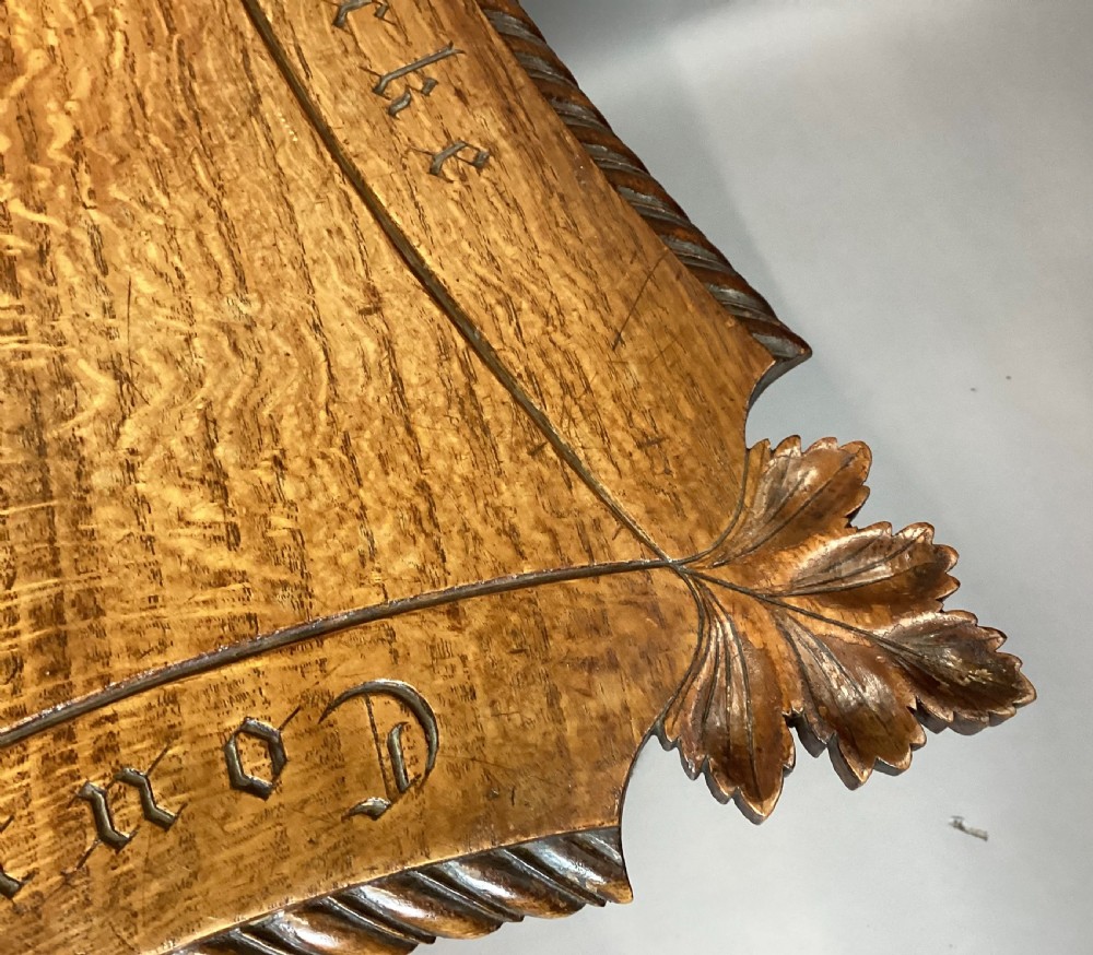 A Regency figured oak occasional table featuring carved acanthus corners, a rope-twist border, incised lettering detail, a turned central stem, and carved legs on castors. View X