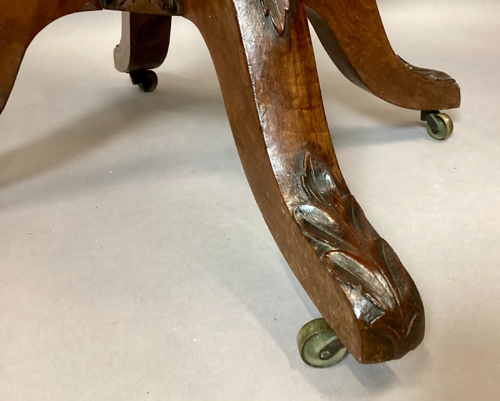 A Regency figured oak occasional table featuring carved acanthus corners, a rope-twist border, incised lettering detail, a turned central stem, and carved legs on castors. View XVII