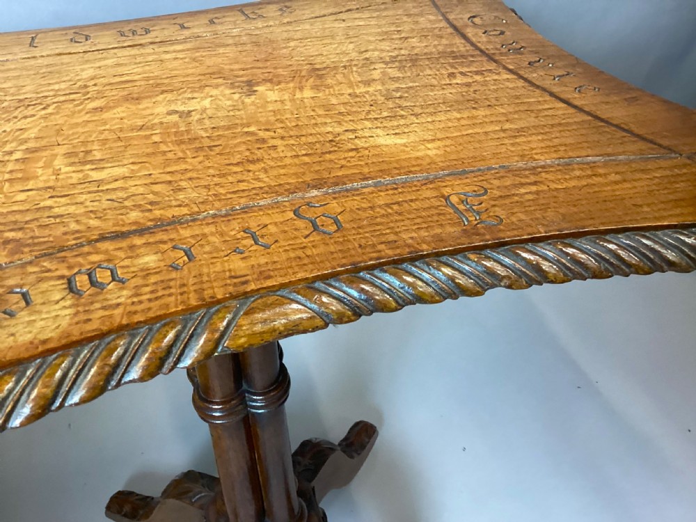 A Regency figured oak occasional table featuring carved acanthus corners, a rope-twist border, incised lettering detail, a turned central stem, and carved legs on castors. View XIX