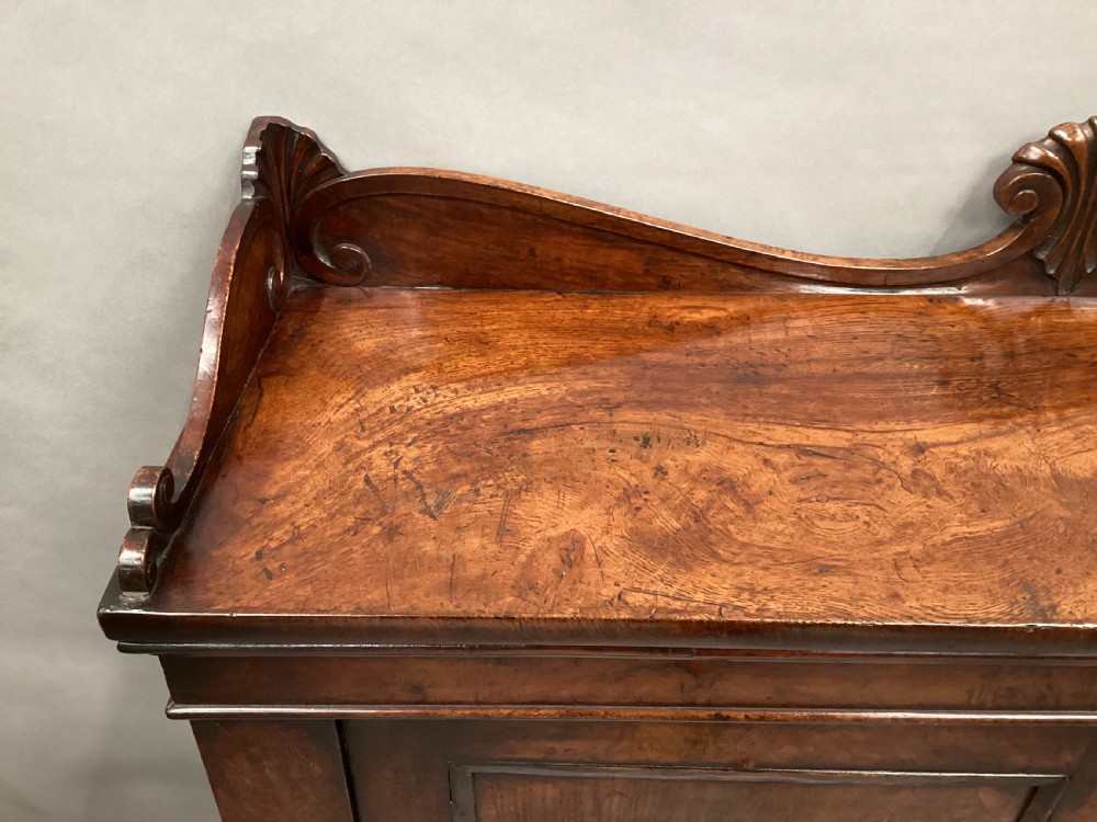 A Regency period side cabinet crafted from figured pollard oak featuring two panelled doors, a carved anthemion upstand, and a plinth base. View XIV